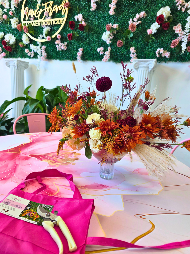 Colorful floral arrangement on a table with a pink tablecloth and a visible brand logo in the background.